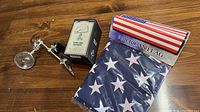 Two items on wooden surface: metal hands-free magnifier with clamp, and packaged American flag.