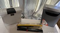 Photo showing the portable file box, long reach stapler in its yellow box, and the compact paper shredder all arranged on a white surface.