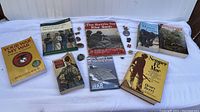Seven vintage military books about the US Marines and related topics displayed on a white fabric surface with seven pins next to the books.