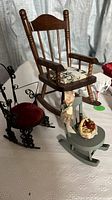 Three miniature rocking chairs in wood, black metal, and grey wood with doll accessories on a white tablecloth.