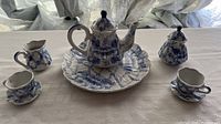 Full set on table: miniature porcelain teapot, sugar bowl, creamer, two cups with saucers on round tray