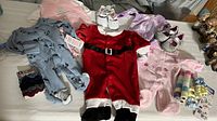 Overview of the baby clothes lot showing multiple footed pajamas, Santa onesie, baby shoes, socks, and accessories arranged on a bed.