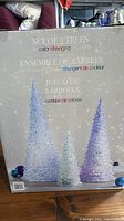Box front showing set of three cone-shaped LED trees with color changing lights in white and shades of purple and green.