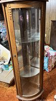 Full view of solid oak and glass corner curio cabinet showing curved glass door and wood frame.