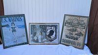 Three vintage metal signs showing U.S. Marines themed designs including a pin-up girl, POW-MIA tribute, and Semper Fi battle scene