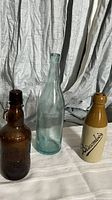 Front view of three vintage bottles: brown Grolsch flip-top, clear glass, and taupe stoneware Discombe bottle.