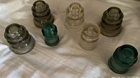 Photo showing all seven vintage glass electric utility insulators laid out on fabric surface. Different shapes and colors are visible.