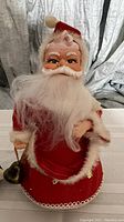 Close-up of vintage Santa music box showing detailed facial features, red velvet suit, and brass bell.