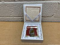 Rainflower stone in acrylic block inside white cushioned box with informational card on lid.