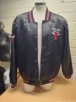 Front view of the black vintage Chicago Bulls satin jacket on a mannequin, showing chest embroidery and snap button closure.