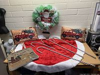 Wide view of Christmas holiday lot including wreath, tree skirt, pillows, candy cane decorations, and nativity sign on a table.