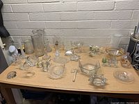 Overview of assorted glass items on wooden table including vases, bowls, and decorative pieces