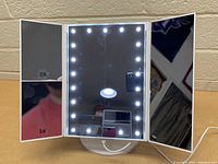 Front view of lighted tri-fold make-up mirror with LED lights around center panel, 2x and 3x magnification mirrors on left panel