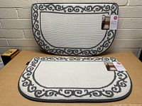 Two new half-round kitchen mats stacked, beige with gray scroll border, tags attached