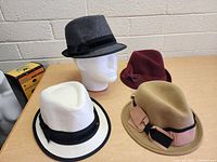Four hats on a table in front of a white brick wall, showing colors and details