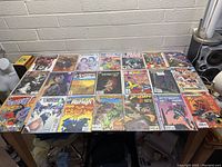 Twenty-four comic books arranged flat on a table, showing front covers including Fantastic Four, Batman, Spider-Man, and others.