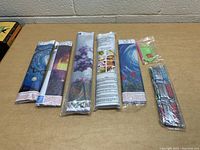 Five unopened diamond bead art kits laid flat showing the rolled printed canvases and small bead bags, including green applicator tool and trays.