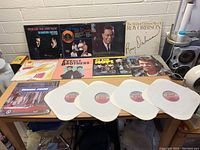 Lot of 9 vinyl records displayed on a table against a wall with various album covers visible, including Roy Orbison, The Platters, Everly Brothers, and others. Four records are visible without sleeves in front.