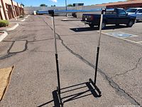 Photo of full rolling adjustable clothing rack showing upright metal frame, horizontal bar, and base with caster wheels.