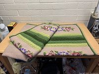 Photo showing the vintage knit blanket folded on a wooden table, displaying green stripes and floral patterns.