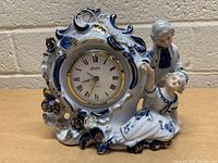 Front view of the vintage Linden mantle clock showing porcelain case with blue and gold detail and figurines of a boy and girl.