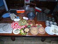 Wide view of entire lot showing various baking pans, cooling racks, trivets, and glassware arranged on wooden table.