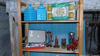Shelving unit displaying all items including turquoise cannisters, boxed melamine dish set, teak napkin holders, cocktail shaker, tumblers and bar utensil set.