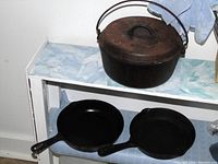 Dutch oven, two frying pans on shelf showing exterior and cooking surfaces