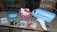 Wide shot of all toys and books on wooden surface showing the Marx Barbie airplane, Hello Kitty light decor, blue typewriter, and four books.