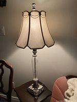 Full view of the decorative lamp with fabric lampshade on a table, lit to show shade texture and lamp height.
