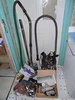 Full view of Filter Queen vacuum with hoses, extension wands, accessories, and a box of filters and other items on floor