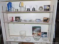 Shelf display showing multiple glass and silverplate items, some in packaging with boxes, including bowls, dishes, candle holders, and decorative pieces.