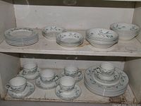 Shelf showing the full set of plates, bowls, cups and saucers in matching wheat pattern decor with blue-green wheat stalks and small blue flowers.