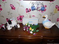 Overview of all items on wooden dresser: bride & groom ceramic set, duck cookie jar, ceramic bread box, and china flowers.