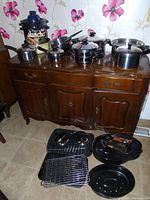 Full view of cookware on wooden buffet and electric hot plates with racks and pans on the floor