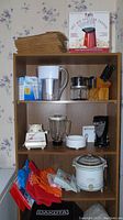 Full view of shelf with kitchen items including popcorn popper box, Brita water pitcher, can opener, crock pot, bags, blender, knives.