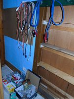 Overall display of electrical cords hanging on the wall with multiple sets of battery charger clamps visible, cords in various colors including black, white, orange, blue, and red.