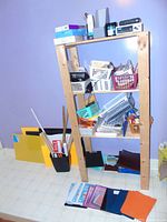 Wide shot of shelving unit with various office supplies in baskets and stacks on shelves and floor.