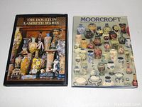 Photo of two hardcover books laid flat; one titled 'The Doulton Lambeth Wares', the other 'Moorcroft' showing various colored pottery items on the covers.