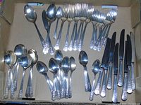 Photo of typical flatware pieces including spoons, forks, and knives grouped by type, showing ornate handles, black handled knives