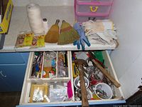 Overview of tools, hardware, string, gloves and whisk brooms laid out in drawers and countertop