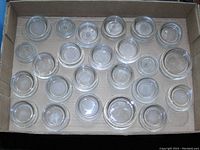 Top view of multiple clear glass furniture coasters arranged in cardboard box, showing varied sizes and mostly uniform design.