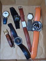 All seven watches laid flat in a box, showing variety of dial styles, strap colors and materials