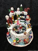 Front view of decorative winter-themed animated music box showing skating children, a squirrel, and snow-covered details around a circular mirror base.