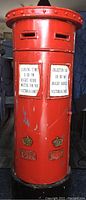 Front full view of the red British mailbox styled CD storage tower showing collection time signs and decorative emblems.