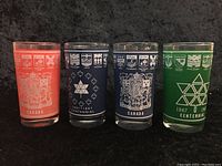 Four cylindrical colored drinking glasses with Canadian Centennial 1867-1967 designs including provincial coats of arms and symbols.