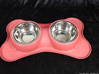 Front view of two stainless steel dog bowls in a pink bone-shaped plastic base.