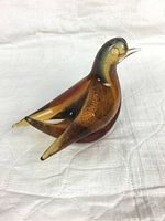 Amber glass bird figurine shown from side perspective on white fabric background.