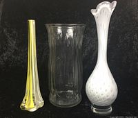 Photo of three glass vases against black background, showing tall light purple vase with white pattern, tall slim yellow vase, and tall clear wide mouth vase.