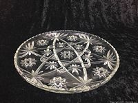 Side angle of large glass tray showing scalloped edge and intricate engraved floral/star pattern on surface.